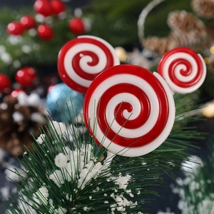 Christmas red and white swirl lollipop ornaments set against snow-covered pine branches