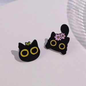 Detail of cute black cat enamel pins with colorful flowers and green leaves on gray surface