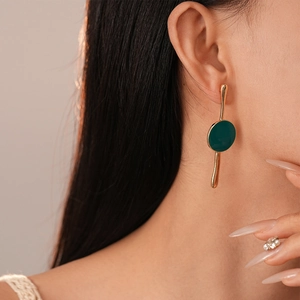 Gros plan d'une boucle d'oreille géométrique dorée avec émail vert foncé sur un modèle