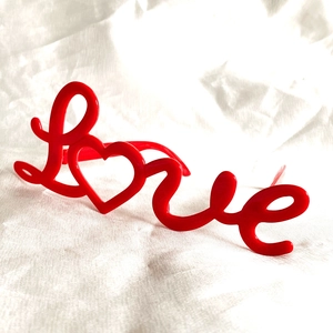 Macro side view of red heart-shaped LOVE letter glasses on white textured fabric