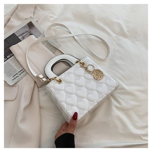 Detailed view of white heart-quilted handbag with gold heart charm on beige blazer