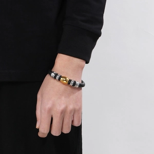 Détail d'un bracelet tressé pour homme avec perle dorée et anneaux métalliques au poignet