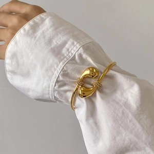 Gepolijste gouden druppelvormige open armband met strass gedragen over een witte mouw