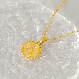 Detail of 18k gold plated round necklace pendant with embossed letter A and textured finish