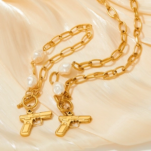 Gold OT buckle pearl necklace with pistol pendant on beige silk background