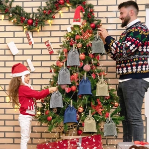 Father and girl hanging linen Christmas advent calendar bags on a decorated tree