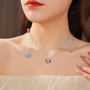 Close-up of blue woven necklace with cartoon dog pendant and floral charms on a model