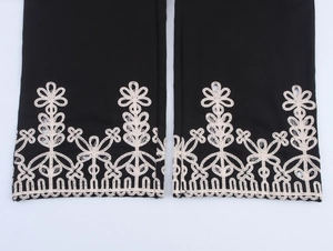 Dettaglio del ricamo floreale traforato bianco sull'orlo dei pantaloni neri larghi