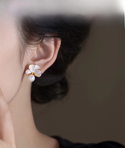 Détail de boucle d'oreille fleur avec perle blanche et bords dorés sur modèle