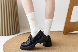 Detailed view of white ribbed crew socks with yellow planet embroidery and loafers