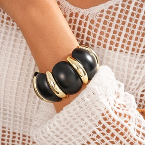 Detail of matte black and polished gold geometric modules on an elastic statement bracelet