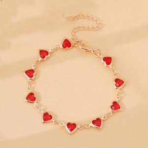 Detailed view of a gold chain bracelet with red heart charms and lobster clasp closure