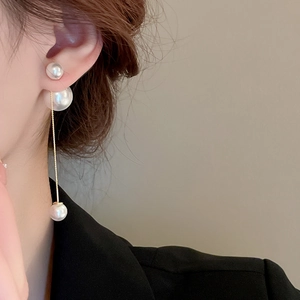 Detail of elegant pearl tassel earrings with gold chain worn by a model in soft light