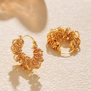 Detail of gold-plated coiled hoop earrings featuring woven textures and zircon stones