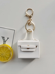Mini white leather handbag keychain with gold hardware on a clean white desk