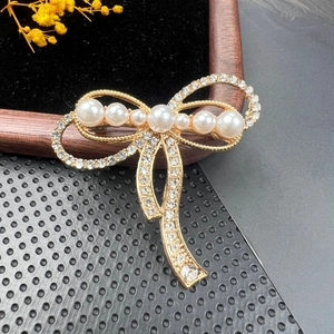 Detailed close-up of a golden bow brooch with elegant pearls and sparkling rhinestones