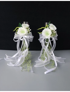 Detail of white artificial flowers with green leaves and organza ribbons on glasses