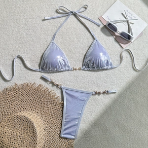 Detail of purple metallic bikini featuring elegant pearl and gold ring accents on woven mat