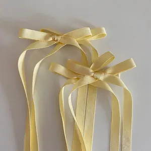Détail de deux nœuds à cheveux en satin jaune pâle avec de longs rubans sur fond blanc