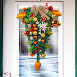 Artificial Christmas teardrop swag with golden ornaments and burlap bow on door