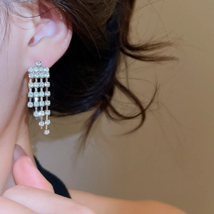 Close-up of sparkling diamond tassel earrings worn by a model in silver finish