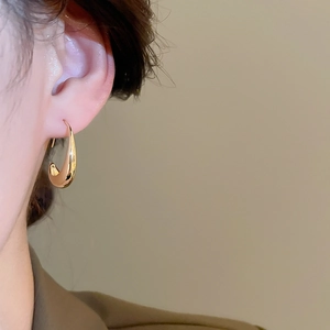 Close-up of 14k gold plated oval drop earrings worn by a model with a polished finish