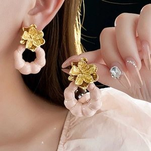 Détail de boucles d'oreilles fleur or vintage avec anneaux roses portées sur fond noir