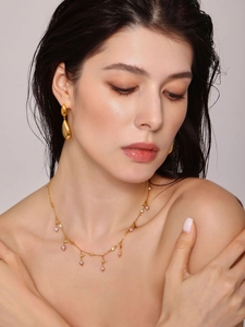 Close-up of golden teardrop earrings and a delicate pearl necklace on a model