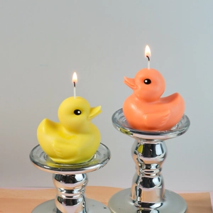 Detail of lit 3D duck candles in yellow and orange on polished silver metal holders
