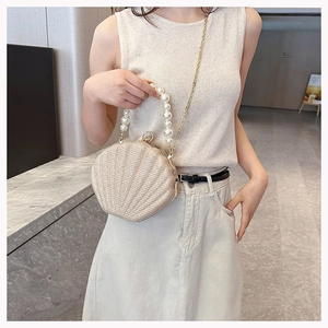 Detail of a beige woven shell bag featuring a pearl handle and gold chain strap