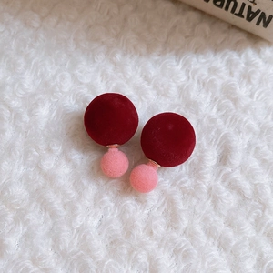 Détail de boucles d'oreilles boules en velours bicolore bordeaux et rose sur tissu blanc