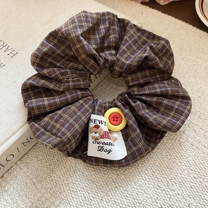 Close-up of brown plaid scrunchie featuring a cartoon dog label and yellow button detail