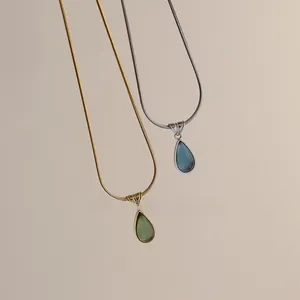 Close-up of gold and silver snake chains with green and blue teardrop crystal pendants