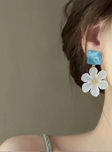 Elegant white acrylic flower stud earrings with blue resin top shown on a model's ear