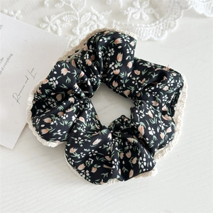 Close-up of black floral fabric scrunchie with beige lace trim on aesthetic background