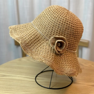 Detail of light brown straw sun hat with wavy brim and floral accent on iron stand