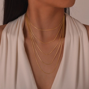 Détail d'un élégant collier à cinq couches en chaîne serpent dorée porté par un mannequin