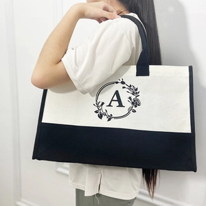 Large white canvas tote bag with black letter A and floral wreath print worn by model