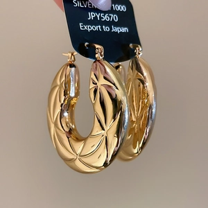 Macro shot of gold hoop earrings featuring geometric star and diamond texture engravings