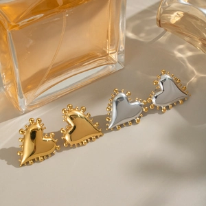 Détail de boucles d'oreilles cœur géométriques en or et argent avec bordure perlée