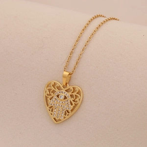 Gold heart pendant necklace with Hamsa hand design and cubic zirconia on beige fabric