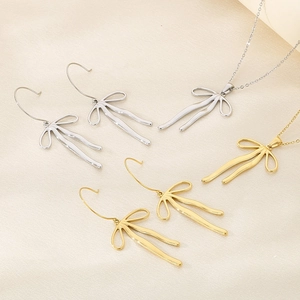 Elegant gold and silver bow pendant necklaces and hook earrings on beige silk fabric