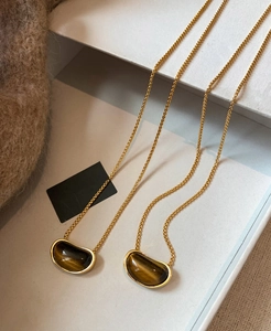 Macro detail of 18k gold plated pea-shaped tiger eye stone pendants on necklaces