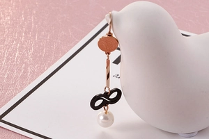 Detail of rose gold earring with black infinity symbol and a white pearl drop