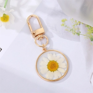 Macro shot of gold leaf-shaped keychain featuring a transparent daisy resin pendant