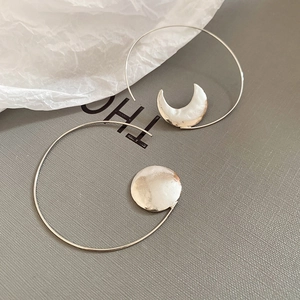 Macro shot of silver asymmetric crescent and sun circular drop earrings on textured paper