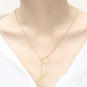 Detail of gold heart and arrow pendant necklace worn over a white shirt for a chic look
