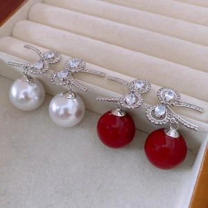 Detail view of bow pearl earrings in red and white colors on a beige velvet jewelry box
