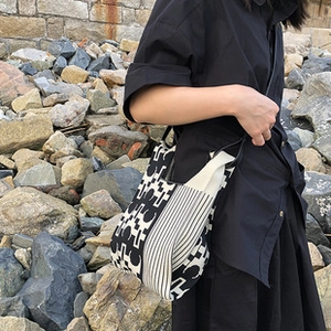 Black and white geometric knitted tote bag shown on shoulder against a rocky background