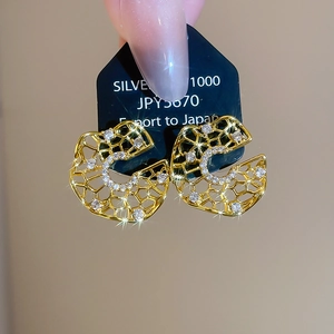 Macro shot of gold-plated C-shaped earrings with hollow honeycomb patterns and zircons